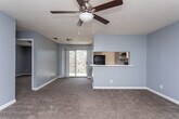 Located at 100 Tallokas Ct in Leesburg, Georgia, this single-floor residence offers a well-organized layout with a cohesive design throughout. The interior is finished in a consistent cool gray-blue palette, complemented by white trim and neutral carpeting across the main living and bedroom areas.

The open living room is generously proportioned, featuring a ceiling fan with light fixture and a textured ceiling. A sliding glass door at the far end floods the space with natural light and provides direct access to an outdoor balcony. The living area connects seamlessly to the kitchen via a pass-through counter, creating an open and communicative floor plan.

The kitchen is fully equipped with black appliances — including a refrigerator, electric range, and dishwasher — set against crisp white cabinetry and white countertops. Tile flooring in a warm beige tone adds durability and easy maintenance to the space.

The bedroom is a comfortable, carpeted retreat with a ceiling fan, a window allowing in natural light, and direct access to a walk-in closet with built-in shelving. An additional bedroom provides similar comfort with carpeted floors and a bright window.

The bathroom features tile flooring matching the kitchen, a single-sink vanity with a mirror, a full soaking tub and shower combo, and cool gray walls that tie the space together with the rest of the home's palette.