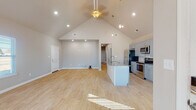 Located at 1000 Zachary St in Centerton, Arkansas, this single-story home showcases a thoughtfully designed open-concept floor plan that seamlessly connects the living, dining, and kitchen areas. The great room is defined by dramatic vaulted ceilings that rise to an impressive peak, complemented by recessed lighting, a ceiling fan, and light wood-look flooring that flows throughout. Natural light filters in through multiple windows fitted with blinds, enhancing the home's airy atmosphere. The kitchen is a functional centerpiece, featuring soft gray shaker-style cabinetry, granite countertops, a center island with a built-in sink, stylish pendant lighting, and a full suite of stainless steel appliances including a refrigerator, range, and over-the-range microwave. The primary bedroom offers a ceiling fan, a walk-in closet with built-in shelving, and direct access to additional rooms. A full bathroom includes a tub/shower combo and a wall-mounted cabinet. The attached garage provides generous storage space, concrete flooring, recessed lighting, an automatic opener, and a dedicated electrical panel. This move-in-ready home delivers a clean, modern aesthetic throughout.