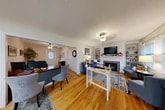 Located at 460 S Main St in North Syracuse, NY, this professionally appointed single-floor office space offers a thoughtfully designed layout comprising four private offices, a bathroom, a closet, and additional rooms suited for various professional uses. Warm hardwood flooring runs throughout, lending a cohesive and inviting character to every area of the space.

The main reception and lounge area immediately sets a welcoming tone, featuring a tile-surround fireplace with a classic white mantel, built-in shelving with crown molding detail, and a mounted flat-screen display. Comfortable upholstered seating in soft blue tones creates an atmosphere reminiscent of a well-appointed living room, making clients feel at ease upon arrival. A front entry area near the glass-panel door provides a functional greeting zone, complete with a console table, mirror, and natural light from a street-facing window.

A private office with a dark wood desk is visible from the main area, offering a quieter workspace separated by a doorway. Further back, an additional office area features fluorescent lighting, hardwood floors, and access to the bathroom and closet. Textured ceilings add dimension throughout, while area rugs help define distinct functional zones. The overall ambiance balances professionalism with warmth, creating a space that is both practical and welcoming for staff and visitors alike.