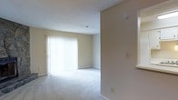 This two-floor residence offers a straightforward and functional layout designed to maximize comfort and usability. The living area, visible in the image, is finished with plush wall-to-wall carpeting in a neutral tone, contributing to a warm and quiet atmosphere. Large sliding glass doors fitted with vertical blinds serve as a prominent feature of the room, allowing an abundance of natural light to fill the space while also providing direct access to an outdoor area. The walls are painted in a soft, neutral beige, complementing the light carpeting and creating a cohesive, understated aesthetic throughout. A textured ceiling adds subtle architectural character to the room. The open sightlines between areas suggest a practical flow between living spaces. A smoke detector is visible, and standard electrical outlets are positioned conveniently along the walls. The two-floor configuration of the residence provides a natural separation between living and private spaces, a layout well-suited for both individuals and households seeking defined zones within the home. Overall, the space presents a clean, move-in-ready environment with an emphasis on natural light and neutral design.