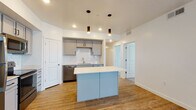 This single-floor unit offers a well-designed, contemporary layout that balances functionality with modern aesthetics. The kitchen serves as a central highlight, featuring gray shaker-style cabinetry, a classic white subway tile backsplash, stainless steel appliances including a refrigerator, range, microwave, and dishwasher, and a light blue island with a clean white countertop. Cylindrical pendant lights hang above the island, adding a stylish touch. Warm wood-look flooring runs throughout the kitchen and main living areas.

The living room is generously sized, bathed in natural light from multiple windows and two sets of French doors, and finished with a ceiling fan and recessed lighting overhead. A separate entry area with a closet and smart lock provides a practical transition space. Bedrooms are carpeted for comfort and include ceiling fans and windows that bring in natural light.

The bathrooms are appointed with gray vanities, white countertops, and wood-look flooring, with one featuring a tub-shower combination. A dedicated laundry room houses a full-size washer and dryer with overhead shelving, adding everyday convenience to this thoughtfully organized space.