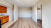 Located on the 12th floor at 5340 Delmar Blvd in St. Louis, Missouri, unit 1203 is a single-floor residence that combines an open, airy layout with practical finishes throughout. The main living area is generously proportioned, featuring light wood-style flooring that runs continuously through the space, bright white walls, and a large picture window that frames sweeping views of the surrounding cityscape and treetops, allowing abundant natural light to fill the room.

The kitchen is positioned adjacent to the living area in a semi-open configuration, separated by a partial wall and a breakfast bar with a wood-tone countertop. It is equipped with warm honey-toned wood cabinetry, a gas range, granite-style countertops, and tile flooring. A window unit provides climate control, and a separate window brings additional natural light into the kitchen area.

The bedroom offers a clean, neutral palette with the same wood-style flooring, a closet, and ample wall space. The bathroom retains a classic design with white subway-style tile wainscoting accented by a light blue tile border, a full soaking tub with shower, a pedestal sink, and a frosted privacy window. The overall ambiance of the unit is bright, clean, and functional, well-suited for comfortable urban living in the Delmar Boulevard corridor.