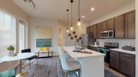 Located at 891 Ingleside Ave in Columbus, Ohio, this single-floor residence offers a thoughtfully designed open-concept layout that blends contemporary style with everyday functionality. The kitchen serves as the centerpiece of the living area, showcasing rich dark cabinetry, a full suite of stainless steel appliances, and a generous white-topped island with pendant lighting overhead — ideal for both meal preparation and casual dining. Wood-look flooring flows seamlessly through the main living spaces, lending warmth and continuity throughout. The living area is bright and inviting, with multiple windows fitted with white blinds that admit generous natural light. Two bathrooms serve the residence: a primary bath featuring a sleek vanity with dark cabinetry, a glass-enclosed shower, and direct access to a walk-in closet with built-in shelving; and a secondary bath equipped with a full soaking tub and shower combination. The bedrooms are carpeted for comfort, offering a cozy retreat with ample natural light from well-placed windows. The overall ambiance of the space is modern and cohesive, with neutral tones, clean lines, and carefully considered finishes that create a welcoming and functional home environment.