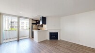 Located at 1616 N Fuller Ave in Los Angeles, Unit 209 is a thoughtfully laid-out single-floor residence that makes efficient use of its compact footprint. The open-concept living and kitchen area features light wood-tone laminate flooring throughout, crisp white walls, and a subtle raised platform section that adds architectural interest and defines separate zones within the shared space. Large vertical blinds cover a sliding glass door, allowing natural light to fill the living area while providing access to an outdoor space.

The kitchen is well-appointed with dark espresso cabinetry extending to the ceiling for ample storage, light quartz countertops, a stainless steel double-basin sink, a full-size stainless steel refrigerator, and a dishwasher. The galley-style layout maximizes functionality within the space.

The unit includes two bathrooms, both finished with the same warm wood-tone flooring. One bathroom features a dark wood vanity with a white quartz countertop, a framed mirror, and chrome fixtures. A separate water closet houses the toilet and includes grab bars, adding accessibility. A dedicated closet completes the layout, providing practical storage solutions for everyday living.