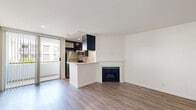Located at 1616 N Fuller Ave in Los Angeles, Unit 209 is a thoughtfully laid-out single-floor residence that makes efficient use of its compact footprint. The open-concept living and kitchen area features light wood-tone laminate flooring throughout, crisp white walls, and a subtle raised platform section that adds architectural interest and defines separate zones within the shared space. Large vertical blinds cover a sliding glass door, allowing natural light to fill the living area while providing access to an outdoor space.

The kitchen is well-appointed with dark espresso cabinetry extending to the ceiling for ample storage, light quartz countertops, a stainless steel double-basin sink, a full-size stainless steel refrigerator, and a dishwasher. The galley-style layout maximizes functionality within the space.

The unit includes two bathrooms, both finished with the same warm wood-tone flooring. One bathroom features a dark wood vanity with a white quartz countertop, a framed mirror, and chrome fixtures. A separate water closet houses the toilet and includes grab bars, adding accessibility. A dedicated closet completes the layout, providing practical storage solutions for everyday living.