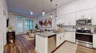 Located at 4220 Colony Plaza Dr in Charlotte's SouthPark area, this single-floor residence offers a thoughtfully designed open-concept layout with contemporary finishes throughout. The kitchen is a standout feature, showcasing crisp white shaker cabinetry extending to the ceiling, granite countertops, a herringbone tile backsplash, stainless steel appliances, and a large center island with bar seating — ideal for both cooking and entertaining. Pendant lighting adds a refined touch overhead, while rich wood-look flooring flows seamlessly throughout the entire unit. The open living area is bright and welcoming, benefiting from natural light through large windows and a glass door that leads to an outdoor space. The bedroom is comfortably proportioned, with large windows, high ceilings, and direct access to the en-suite bathroom. The bathroom features a dual-sink granite vanity with dark cabinetry, a soaking tub, and floor-to-ceiling subway tile work, creating a clean and spa-like atmosphere. Throughout the residence, a neutral color palette, elevated ceiling heights, and cohesive modern design elements contribute to an overall ambiance that is both polished and comfortable.