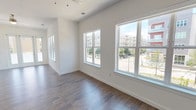 Located at 3451 N Plano Rd in Richardson, Texas, this single-floor unit showcases a clean, contemporary design with an open and airy layout throughout. The main living area is defined by large double-hung windows that frame views of the surrounding urban community, allowing abundant natural light to fill the space. Dark hardwood-style flooring runs throughout the living and dining areas, adding warmth and contrast to the bright white walls and trim. A ceiling fan is centrally positioned overhead, contributing to both comfort and visual balance.

The kitchen is well-appointed with gray flat-panel cabinetry, white quartz countertops, a white subway tile backsplash, and a full suite of stainless steel appliances including a range, over-the-range microwave, dishwasher, and refrigerator. A peninsula with a stainless steel sink and pendant lighting connects the kitchen to the open living space.

Bedrooms feature plush neutral carpet, individual windows for natural light, and access to closet storage. The primary bathroom offers a dual-sink vanity with a wide framed mirror, white quartz countertops, slate-blue cabinetry, and tile flooring, delivering a polished, modern finish. The overall ambiance is bright, clean, and move-in ready.