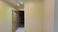 This single-floor space is characterized by its warm, yellow-toned walls that create an inviting atmosphere throughout. A standout feature is the wood-framed door fitted with frosted glass panels, offering a balance of privacy and light diffusion while adding a refined design element to the interior. Beyond the door, a built-in shelving unit is visible, constructed from dark wood and offering multiple tiers of storage — suggesting this area functions as a dedicated storage or wardrobe space. The ceiling incorporates recessed lighting, providing focused, even illumination across the space. The light-colored tiled flooring complements the warm wall tones, contributing to a cohesive and clean aesthetic. The overall layout appears compact yet efficiently designed, with thoughtful use of built-in storage to maximize functionality. The combination of wood accents, frosted glass, and warm wall colors gives the space a cozy yet practical character suitable for everyday use.