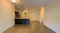 Located at 1821 Buckeye Drive in Richmond Hill, Georgia, this single-floor residence offers a thoughtfully designed open-concept layout that promotes a sense of spaciousness and easy flow between living areas. The kitchen serves as a central focal point, anchored by a dark, substantial island with a granite countertop and an undermount sink, providing ample workspace and a natural gathering spot. Dark cabinetry lines the kitchen walls, complemented by stainless steel appliances including a refrigerator and microwave. Recessed lighting throughout the kitchen and living areas ensures consistent, bright illumination, while a stylish pendant light hangs above the island, adding a decorative touch. The flooring throughout the main living space is a warm-toned hardwood, lending a cohesive and polished look. The open living area extends generously from the kitchen, bathed in warm ambient light. Multiple doorways lead to additional rooms, hinting at a functional and well-organized floor plan. The neutral wall tones and clean architectural lines throughout contribute to a bright, welcoming atmosphere well-suited for both everyday living and entertaining.