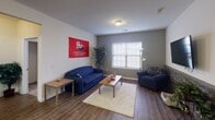 Located near Shippensburg University in Shippensburg, PA, this single-floor residence offers a functional and comfortable layout well-suited for student living. The living room serves as a welcoming common area, featuring wood-look flooring, neutral and gray accent walls, large windows that invite natural light, and ample space for seating and relaxation. The kitchen is equipped with oak cabinetry, dark granite countertops, a striking stone-tile backsplash, and black appliances including a range and over-the-range microwave. Multiple carpeted bedrooms provide private retreats, each with a window for natural light, dedicated desk space for studying, and room for a bed. The bathrooms are clean and practical, featuring tile flooring, a vanity with an oval mirror, and bright overhead lighting. A dedicated laundry area houses a full-size washer and dryer alongside overhead wire shelving for storage. Hallways connect the rooms with ease, offering an efficient flow throughout the single-story floor plan. This residence combines practical amenities with a comfortable layout, making it a well-rounded option for those seeking housing convenient to the Shippensburg University campus.