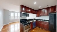 Located at 10 N Sheridan Rd in Waukegan, Illinois, this one-bedroom, one-bathroom unit offers a well-organized layout with consistent hardwood flooring throughout, lending warmth and continuity across every room.

The combined kitchen and living area forms the heart of the unit. The kitchen is thoughtfully designed with rich, dark cherry wood cabinetry extending to the ceiling for ample storage, dark granite countertops, stainless steel appliances including a range, microwave, and dishwasher, and a pass-through breakfast bar that opens to the living space. Recessed lighting and natural light from adjacent windows keep the area bright and functional.

The living room benefits from the open connection to the kitchen, offering a comfortable and versatile space with clean grey walls and polished hardwood floors.

The bedroom is a well-proportioned retreat featuring a large triple-pane window that frames sweeping elevated views of the surrounding Waukegan landscape. The room's light grey walls and gleaming hardwood floors create a calm, airy atmosphere. A closet provides dedicated storage.

The bathroom is finished with large-format stone tile on both the floor and tub surround, complemented by chrome fixtures and a clean white palette, giving it a polished and durable finish.