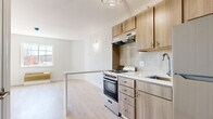 Located at 1151 E Main St in Meriden, Connecticut, this single-floor residence showcases a clean, contemporary design with light hardwood flooring throughout, creating a bright and cohesive aesthetic across every room.

The open-concept kitchen is a standout feature, outfitted with warm-toned wood cabinetry, brushed nickel hardware, a white quartz peninsula countertop, a gas range with stainless steel appliances including a refrigerator, a single-basin sink, and a textured tile backsplash. A stylish pendant light fixture anchors the space, while the peninsula provides a natural division between the kitchen and the living area. The living space benefits from natural light streaming through a multi-pane window with views of the surrounding landscape.

The bedroom is generously proportioned, featuring light-washed hardwood floors, a rich dark accent wall with a textured finish, and direct access to the bathroom. Natural light fills the room through well-positioned windows.

The bathroom is elegantly appointed with large-format dark marble-style floor tiles, a combination tub and shower, a wall-mounted vanity with a white countertop and integrated sink, a backlit mirror, and a decorative 3D-textured tile wall that adds a sophisticated touch.

Overall, this residence offers a modern, move-in-ready living environment with quality finishes and a functional layout.
