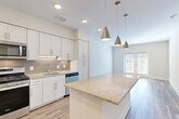 Located at 20725 Wood Quay Dr in Sterling, VA, this thoughtfully designed one-bedroom, one-bathroom residence offers a bright and efficient single-floor layout. The open-concept kitchen and living area serves as the heart of the home, where crisp white shaker cabinetry, a taupe subway tile backsplash, and a generous granite-topped island create a functional yet stylish centerpiece. Three brushed nickel pendant lights hang above the island, complementing the stainless steel appliances — including a gas range, microwave, refrigerator, and dishwasher. Light wood-tone flooring extends throughout the main living area, which is bathed in natural light from a set of glass French doors. The bedroom features plush carpet flooring, neutral walls, and a window with exterior views, offering a calm and comfortable retreat. The full bathroom is finished with classic white subway tile surrounding the soaking tub and shower, tile flooring, and granite vanity accents. A dedicated laundry area accommodates a stacked washer and dryer unit, adding everyday convenience. Additional spaces include a hallway, closet, and utility room, ensuring practical storage and circulation throughout.