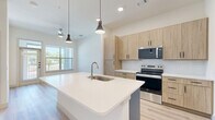 Located in Lewisville, TX, this well-designed one-bedroom, one-bathroom unit offers a clean, modern aesthetic across its thoughtfully arranged single floor. Light wood-look flooring flows seamlessly throughout, complementing the crisp white walls and creating a bright, cohesive atmosphere.

The kitchen serves as a central highlight, featuring a large island with a white quartz countertop, an undermount sink, and pendant lighting overhead. Light wood cabinetry pairs with stainless steel appliances — including a refrigerator, range, microwave, and dishwasher — and a classic white subway tile backsplash adds a refined touch.

The bedroom is a comfortable, well-proportioned retreat bathed in natural light from large windows with outdoor views. Ceiling fans in both the main living area and bedroom enhance year-round comfort. An adjacent walk-in closet provides generous storage with dual hanging rods and shelving along the walls.

The bathroom is finished with warm wood-tone cabinetry, a white quartz vanity top, a large mirror, and a full soaking tub with tiled surround. The continued light wood flooring ties the space together with consistency and style. The overall ambiance is clean, contemporary, and move-in ready.