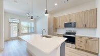 Located in Lewisville, TX, this well-designed one-bedroom, one-bathroom unit offers a clean, modern aesthetic across its thoughtfully arranged single floor. Light wood-look flooring flows seamlessly throughout, complementing the crisp white walls and creating a bright, cohesive atmosphere.

The kitchen serves as a central highlight, featuring a large island with a white quartz countertop, an undermount sink, and pendant lighting overhead. Light wood cabinetry pairs with stainless steel appliances — including a refrigerator, range, microwave, and dishwasher — and a classic white subway tile backsplash adds a refined touch.

The bedroom is a comfortable, well-proportioned retreat bathed in natural light from large windows with outdoor views. Ceiling fans in both the main living area and bedroom enhance year-round comfort. An adjacent walk-in closet provides generous storage with dual hanging rods and shelving along the walls.

The bathroom is finished with warm wood-tone cabinetry, a white quartz vanity top, a large mirror, and a full soaking tub with tiled surround. The continued light wood flooring ties the space together with consistency and style. The overall ambiance is clean, contemporary, and move-in ready.
