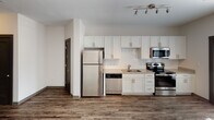 Located at 726 Fulton St in Chattanooga, Tennessee, this single-floor unit offers a thoughtfully designed open-concept layout with modern finishes throughout. The entryway welcomes you with light-toned luxury vinyl plank flooring that flows seamlessly into the main living and kitchen areas, creating a cohesive and airy feel.

The kitchen is a standout feature, outfitted with white shaker cabinetry, granite-style countertops, a classic white subway tile backsplash, and a full suite of stainless steel appliances, including a refrigerator, electric range, over-the-range microwave, and dishwasher. Track lighting overhead adds both style and functionality to the space.

The open living area is bright and inviting, benefiting from natural light streaming through a large window and glass French doors that lead to an outdoor area. A ceiling fan enhances comfort in the living space. The darker hardwood-style flooring in this area adds warmth and contrast to the clean white walls.

The bedroom features soft carpeting and neutral tones, offering a calm and restful environment. The bathroom is well-appointed with a white vanity, granite countertop, modern fixtures, and wood-look flooring that ties the overall design together. Additional storage is provided by a louvered-door closet near the entry. This unit combines clean, contemporary aesthetics with practical amenities in a convenient Chattanooga location.