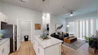 Located at 1619 N Frazier Street in Conroe, TX, this thoughtfully designed 2-bedroom, 2-bathroom single-story residence offers a modern open-concept layout with wood-look flooring throughout the main living areas. The kitchen is a standout feature, showcasing white shaker cabinetry extending to the ceiling, granite countertops, stainless steel appliances, and a central island with bar seating — all illuminated by sleek pendant lighting. The kitchen flows seamlessly into the living room, which benefits from tall ceilings, large windows that invite abundant natural light, and a ceiling fan for added comfort. A dedicated in-unit laundry closet with a stacked washer and dryer adds everyday convenience. Both bathrooms are finished with granite-topped white vanities and wood-look flooring; one features a tub-shower combination with tile surround. The primary bedroom offers a comfortable, carpeted retreat with a closet, natural light through slatted windows, and a calm, neutral color palette. The second bedroom is equally well-appointed with a closet and natural light. Two hallways connect the spaces efficiently, completing a well-organized and modern floor plan.