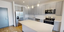 Unit 203 at 1201 is a thoughtfully designed one-bedroom, one-bathroom apartment encompassing 660 square feet of single-floor living space. The open-concept kitchen and living area serves as the heart of the unit, showcasing light hardwood flooring that extends throughout. The kitchen is well-appointed with gray shaker-style cabinetry, white quartz countertops, a large center island with pendant lighting, stainless steel appliances including a refrigerator, range, microwave, and dishwasher, and recessed lighting overhead. The living area flows seamlessly from the kitchen and provides direct access to a private balcony through sliding glass doors, offering views of the surrounding residential community. A dedicated window also brings in additional natural light. The bedroom measures 140 square feet and features a large window with neighborhood views, light hardwood flooring, and clean white walls. The bathroom includes a wide vanity with white quartz countertops, gray cabinetry, a large mirror, a walk-in shower, and matching hardwood-style flooring. A closet provides added storage. The unit maintains a clean, contemporary aesthetic with neutral tones and modern finishes throughout.