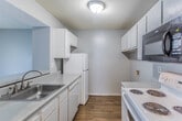 This single-story residence in Memphis, Tennessee offers a practical and comfortable layout across two bedrooms and two bathrooms. The living area is finished with warm wood-look hard flooring and painted in a soft blue-gray palette, creating a clean, neutral ambiance throughout. A half-wall partition separates the living space from the adjacent kitchen area, which features white cabinetry and includes a full-size refrigerator. A dedicated laundry area with overhead cabinetry and washer/dryer connections adds everyday convenience.

Sliding glass doors in the living area open to an outdoor space, allowing natural light to filter in and providing easy exterior access. The bedrooms are carpeted for comfort and painted in the same cool gray tones. The primary bedroom benefits from dual windows, offering ample natural light, and includes direct access to a private en-suite bathroom as well as a walk-in closet. The second bedroom also features a window with a view of the outdoors. Textured ceilings are consistent throughout the unit. Overall, the space presents a straightforward, functional design well-suited for everyday living in the Memphis area.