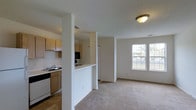 This single-floor 1-bedroom, 1-bathroom residence offers a practical and well-organized layout designed for comfortable everyday living. The open-concept design connects the kitchen and living area seamlessly, creating a cohesive and functional flow throughout the space. The kitchen is outfitted with light wood cabinetry, a black range, a dishwasher, a refrigerator, and a sink with ample counter space. A half-wall partition defines the kitchen without fully enclosing it, maintaining an open and airy feel. The adjoining living area features neutral wall-to-wall carpeting that adds warmth underfoot, while a pair of windows along the far wall invites natural light and provides views of the outdoors. The clean white walls and simple ceiling fixtures contribute to a bright, understated ambiance throughout. The tile flooring in the kitchen transitions smoothly into the carpeted living space, offering both practicality and comfort in their respective zones. Overall, this residence presents a straightforward, move-in-ready layout that balances functionality with a welcoming atmosphere.