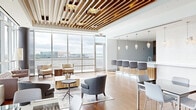 Located in McLean, Virginia, this elegantly designed single-floor space offers a seamless blend of modern architecture and upscale finishes. The interior is immediately distinguished by its dramatic slatted wood ceiling with integrated crystal chandeliers, which runs throughout the main areas and adds warmth and visual depth overhead. Wide-plank hardwood flooring flows throughout, grounding the contemporary aesthetic.

Floor-to-ceiling glass curtain walls wrap around the space, flooding every area with abundant natural light and offering sweeping panoramic views of the surrounding McLean and greater Northern Virginia skyline. A spacious living area features multiple seating arrangements, including lounge chairs and sofas, ideal for relaxed gathering. The adjacent dining area accommodates a large, generously sized table surrounded by upholstered chairs, positioned to take full advantage of the expansive views.

The kitchen is outfitted with rich wood cabinetry, white quartz countertops, a large island with bar seating, and elegant pendant lighting. A separate glass-enclosed dining nook opens directly to an expansive outdoor terrace, finished in large-format tile and framed by bold structural columns, providing an exceptional open-air setting above the treetops. Together, these spaces create a refined, versatile environment suited for both intimate gatherings and large-scale entertaining.