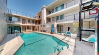 This multi-story residential complex is designed around a central courtyard that serves as the focal point of the property. At the heart of the outdoor space is a generously sized swimming pool with crystal-clear turquoise water, surrounded by a well-maintained tiled deck ideal for lounging and recreation. The pool area is equipped with seating, including modern lounge chairs, and is enclosed by sleek glass fencing that maintains an open, airy feel while ensuring safety.

The building's architecture features a contemporary design with neutral-toned stucco and stone cladding facades, large windows, and sliding glass doors that open directly onto the courtyard from ground-floor units. Upper floors are accessed via a striking open metal staircase and feature wraparound walkways with black metal railings, offering residents elevated views of the pool and courtyard below. Private balconies on the upper levels extend the living space outdoors, enhancing the indoor-outdoor lifestyle the property promotes.

The courtyard is bathed in natural sunlight throughout the day, creating a bright and inviting atmosphere. Ground-level units benefit from direct pool access through sliding glass doors, seamlessly blending interior and exterior living. The overall ambiance is modern, clean, and resort-like, making the shared outdoor amenity a central feature of the community experience.
