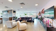 This thoughtfully designed single-floor amenity space offers a dynamic blend of comfort, functionality, and eclectic style. The open-plan layout is anchored by expansive floor-to-ceiling windows that flood the interior with natural light and frame panoramic city views, creating an airy, elevated atmosphere throughout.

The main lounge area is generously proportioned, featuring a large sectional sofa, rounded accent chairs in neutral tones, and a coffee table set atop polished concrete floors. One wall serves as a bold focal point, finished in soft pink and adorned with an eclectic gallery wall of signage, artwork, and decorative objects, adding a playful and curated character to the space.

A sleek wet bar with a long white countertop, bar stools, and a textured striped accent wall with an inset television provides an ideal setting for social gatherings. Adjacent seating nooks with curved lounge chairs and tall tropical plants offer more intimate conversation areas with direct window views of the cityscape.

A dedicated fitness room, visible through glass-paneled doors, houses cardio equipment and exercise balls, keeping wellness seamlessly integrated into the space. Lush greenery is distributed throughout, softening the modern aesthetic and enhancing the welcoming ambiance. Recessed ceiling lighting and a centralized HVAC system ensure year-round comfort across the entire floor.