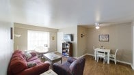 This single-story home offers three bedrooms and two bathrooms across a practical, well-organized floor plan. The living area is a comfortable, open space featuring hardwood-style flooring that extends throughout the main areas, creating a cohesive and easy-to-maintain surface. A large window along one wall allows natural light to fill the room, brightening the neutral beige walls and textured ceiling. The living room accommodates generous seating arrangements and includes a ceiling fan for added comfort.

The space flows naturally into a dedicated dining area, which is defined by its own ceiling fan overhead and offers room for a full dining set. A bookcase and media storage unit provide functional organization within the living space, keeping entertainment essentials accessible. The open connectivity between the living and dining areas enhances the sense of space, making the layout well-suited for everyday living and casual entertaining. The overall ambiance is warm and understated, with a straightforward design that prioritizes functionality and livability throughout the single-floor layout.