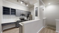 This thoughtfully designed one-bedroom, one-bathroom residence offers an efficient and modern layout across a single floor, accessed via a carpeted staircase with a sleek metal handrail. The open-concept living area features light wood-look flooring, crown molding, and a ceiling fan, creating a bright and welcoming atmosphere. Large windows and a sliding glass door allow natural light to fill the space while providing outdoor views.

The kitchen is a standout feature, equipped with gray shaker-style cabinetry, open shelving, white subway tile backsplash, white quartz countertops, and a full suite of stainless steel appliances including a range, microwave, refrigerator, and dishwasher. A peninsula counter offers additional prep space and a casual dining option.

The bedroom is generously proportioned with vaulted ceilings, a ceiling fan, wood-look flooring, and a sliding glass door that opens to an outdoor area. A dedicated walk-in closet provides ample storage with built-in shelving and hanging rods. The bathroom includes a soaking jetted tub with tile surround, gray cabinetry with updated hardware, and light wood-look flooring. A separate laundry area adds everyday convenience, completing this well-appointed and functional living space.