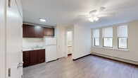This efficiently designed single-floor studio offers a well-considered layout that maximizes every square foot. The open main living area features light-toned hardwood-style flooring that runs throughout the space, creating a cohesive and clean aesthetic. A ceiling fan with integrated lighting anchors the living area, providing both airflow and illumination. A bank of three windows along one wall floods the space with natural light while offering views of the surrounding neighborhood, complemented by baseboard heating beneath for year-round comfort.

The kitchen is neatly appointed with rich dark-wood cabinetry that extends to the upper walls for ample storage. White appliances, including a full-size refrigerator and gas range, are set against light countertops, creating a functional and tidy cooking space. Recessed lighting above keeps the kitchen well-lit. Two closet doors flank the kitchen entrance, providing convenient storage options.

The bathroom is clean and straightforward, featuring a full-size soaking tub with a white subway-tiled surround and overhead shower. A single window allows natural light into the space, while a vanity with under-sink storage and wood-style flooring complete the room. The overall ambiance of the studio is practical and bright, ideal for efficient, comfortable living.