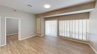This single-floor space presents a clean, modern aesthetic carried consistently throughout. The kitchen serves as a standout feature, boasting dark espresso cabinetry with sleek bar-pull hardware, stone-look countertops, and a full suite of stainless steel appliances including a refrigerator, range, microwave, and dishwasher. Track lighting overhead highlights the space's contemporary character, while an open island provides additional prep and seating space. A built-in pantry with open shelving adds practical storage. Light wood-look flooring flows seamlessly throughout the entire unit, contributing to a cohesive and airy feel. The living area is generously sized, featuring large sliding glass doors and wide windows fitted with blinds that invite abundant natural light. The bedroom offers a calm, neutral palette with soft gray walls, wood-look flooring, and a window with blinds for natural illumination. The bathroom is thoughtfully designed with a combination tub and shower enclosed by a glass sliding door, large-format white wall tiles, a dark vanity with a stone countertop, and matching wood-look flooring that ties the space together. Clean lines and a neutral color palette throughout lend the space a polished, contemporary character.
