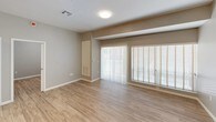 This single-floor space presents a clean, modern aesthetic carried consistently throughout. The kitchen serves as a standout feature, boasting dark espresso cabinetry with sleek bar-pull hardware, stone-look countertops, and a full suite of stainless steel appliances including a refrigerator, range, microwave, and dishwasher. Track lighting overhead highlights the space's contemporary character, while an open island provides additional prep and seating space. A built-in pantry with open shelving adds practical storage. Light wood-look flooring flows seamlessly throughout the entire unit, contributing to a cohesive and airy feel. The living area is generously sized, featuring large sliding glass doors and wide windows fitted with blinds that invite abundant natural light. The bedroom offers a calm, neutral palette with soft gray walls, wood-look flooring, and a window with blinds for natural illumination. The bathroom is thoughtfully designed with a combination tub and shower enclosed by a glass sliding door, large-format white wall tiles, a dark vanity with a stone countertop, and matching wood-look flooring that ties the space together. Clean lines and a neutral color palette throughout lend the space a polished, contemporary character.