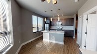 This contemporary single-floor unit offers a well-designed open-concept layout that seamlessly connects the living and kitchen areas. The kitchen is a standout feature, showcasing rich dark wood cabinetry, a white quartz countertop, a subway tile backsplash, and a full suite of stainless steel appliances including a refrigerator, electric range, and over-the-range microwave. A central island with an integrated sink and matte black faucet serves as both a functional workspace and a casual gathering point, illuminated by elegant pendant lighting and complemented by track lighting overhead. Wood-look flooring flows throughout the main living areas, adding warmth and continuity to the space. Large windows fitted with horizontal blinds invite generous natural light throughout, with views of the surrounding urban streetscape. The bedrooms are carpeted for comfort, each equipped with a ceiling fan and ample closet space, including a sliding-door closet with built-in wire shelving. The bathrooms are thoughtfully finished, with one featuring a full tub-shower combo with matte black fixtures, and another offering a navy blue vanity with a white countertop, a lighted mirror, and wood-look flooring. Neutral gray wall tones throughout the unit create a cohesive, modern aesthetic.