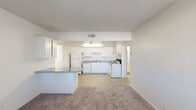 This single-floor unit offers a clean, functional layout designed for comfortable everyday living. The open-concept living and kitchen area serves as the heart of the space, where a peninsula with a speckled blue countertop separates the carpeted living area from the kitchen. The kitchen is outfitted with white cabinetry providing ample upper and lower storage, granite-look laminate countertops, a double stainless steel sink, and white appliances including a refrigerator, electric range, and dishwasher. Light wood-look flooring runs throughout the kitchen, adding a warm contrast to the bright white cabinetry. A textured popcorn ceiling and overhead lighting complete the kitchen's functional design.

The bedrooms are carpeted and finished with neutral walls and textured ceilings. Each room features a window fitted with vertical blinds, allowing for natural light and privacy. The layout includes two bathrooms, each featuring a tiled tub and shower combination, a toilet, light wood-look flooring, and clean white walls. Both bathrooms are simply appointed, offering a practical and easy-to-maintain design. Overall, the space presents a straightforward, well-maintained layout suited to a range of occupants.