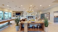 This well-appointed single-floor clubhouse offers a thoughtfully designed layout that blends social, recreational, and functional spaces seamlessly. The main lounge serves as the centerpiece, featuring a linear fireplace clad in herringbone-patterned tile, framed by mirror-paneled columns that amplify the sense of space. A statement brass chandelier with cylindrical glass accents anchors the room, while light hardwood flooring and neutral tones create a bright, welcoming ambiance. Plush seating arrangements, decorative greenery, and curated artwork contribute to an elevated, resort-style atmosphere.

Adjacent to the lounge, a wet bar and café station is equipped with a Keurig coffee setup, under-counter beverage refrigerator, stainless steel sink, and open shelving against a hexagonal mosaic tile backsplash—ideal for casual entertaining. A dedicated business center provides a quiet workspace with multiple computer workstations, patterned carpet, and soft blue walls.

The game room offers a more relaxed setting, featuring a shuffleboard table, leather club chairs, and multiple wall-mounted televisions. Nearby, a transitional lounge area includes an arcade game, additional seating, and access to outdoor views through large windows, inviting natural light throughout the space.