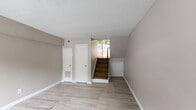 Located at 5320 Roswell Rd in Sandy Springs, GA, this one-bedroom, one-bathroom two-story unit offers a practical and functional layout across two floors. The main level features a welcoming living area with light-toned hardwood-style flooring, neutral warm-beige walls, and a textured ceiling that carries throughout the space. Natural light filters in through a window overlooking greenery, creating a bright and airy feel. A sloped-ceiling area on the main level adds a subtle architectural detail and additional usable space, also finished with the same clean hardwood-style flooring. The unit includes a dedicated hallway connecting the living areas to the upper floor. Upstairs, the carpeted bedroom offers a comfortable retreat, complete with a ceiling fan with light fixture, a generous bi-fold door closet, and a window that brings in natural light. Neutral gray-toned walls give the bedroom a calm, relaxed atmosphere. The full bathroom is finished with white tile in the tub/shower surround, mosaic tile flooring, and warm beige walls, providing a clean and functional space. Throughout the unit, consistent neutral tones and clean finishes create a cohesive and move-in-ready environment.