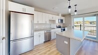 Located at 231 Scarborough Downs Rd in Scarborough, Maine, this well-designed 2-bedroom, 1-bathroom single-floor residence offers a comfortable and modern living experience. The open-concept layout connects the kitchen and living area seamlessly, creating an inviting and functional space. The kitchen is a standout feature, boasting white shaker cabinetry extending to the ceiling, granite countertops, a granite-topped island with pendant lighting, and a full suite of stainless steel appliances including a refrigerator, electric range, microwave, and dishwasher. Light wood-tone luxury vinyl plank flooring runs throughout the main living areas and hallway, adding warmth and continuity. The bright living room benefits from large windows that flood the space with natural light and offer outdoor views of the surrounding Scarborough area. Both bedrooms feature plush carpet flooring, generous closet space — including a walk-in closet in the primary bedroom — and neutral wall tones. The bathroom is finished with a white vanity, large mirror, and LVP flooring. A dedicated laundry room with wire shelving and utility hookups adds convenience. The clean, modern aesthetic throughout is defined by white trim, recessed lighting, and a cohesive neutral color palette.