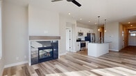 This two-story home showcases a clean, modern design throughout its well-appointed layout. The main living area features light-toned luxury vinyl plank flooring, a ceiling fan, and a sleek glass-front fireplace with a minimalist concrete surround, anchoring the open-concept living space. The kitchen is thoughtfully designed with white shaker cabinetry, stainless steel appliances including a gas range, microwave, refrigerator, and dishwasher, complemented by granite countertops and a undermount sink on the island peninsula. Pendant lighting adds warmth above the island, which also provides additional seating and prep space. A bright hallway with recessed lighting connects the main living areas to additional rooms, including a well-sized bedroom featuring plush carpeting, a ceiling fan, and a large window offering outdoor views. A dedicated laundry room includes a washer and dryer with wire shelving, while a spacious walk-in closet provides ample wire-rack storage. A bathroom with tile flooring and a grab bar offers functional accessibility. The unfinished basement presents flexible potential, with framed walls, insulated concrete walls, and concrete flooring ready for future finishing.