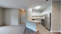 Located at 7703 Lee Rd in Lithia Springs, Georgia, this single-floor residence offers a practical and well-appointed layout with a clean, neutral aesthetic throughout. The open-concept living and kitchen area serves as the heart of the home, where wood-look flooring flows seamlessly underfoot. The kitchen is outfitted with white shaker-style upper cabinets, light gray lower cabinets, granite-look countertops, a subway tile backsplash, and a full suite of stainless steel appliances including a refrigerator, range, and dishwasher. A peninsula with a rounded breakfast bar provides additional counter space and casual seating. The living area transitions naturally from the kitchen, with a front entry door visible from the common space. Bedrooms are carpeted for comfort and feature ceiling fans, ample natural light from windows with blinds, and access to closet space. The bathroom includes a full tub-shower combo with white tile surround and wood-look flooring. Textured ceilings are present throughout, and soft gray walls provide a consistent, neutral backdrop across all rooms. The layout is efficient and functional, making thoughtful use of the available space on a single level.