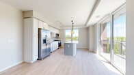 Located at 130 N Haven Rd in Elmhurst, IL, this well-appointed three-bedroom, two-bathroom residence offers a thoughtfully designed single-floor layout with a bright and contemporary aesthetic. The open-concept kitchen and living area serves as the heart of the home, featuring white shaker cabinetry, stainless steel appliances including a gas range, built-in microwave, and French door refrigerator, paired with a central island and a pendant light fixture. Large windows flood the space with natural light and offer pleasant views of the surrounding greenery. Light-toned hardwood flooring runs throughout the main living areas, creating a cohesive and airy feel. A well-lit hallway with recessed lighting connects the living spaces to the private bedroom wing, where plush carpeting adds warmth underfoot. The primary bedroom is generously sized and includes a window for natural light. The bathrooms are finished in a clean, modern style — one featuring large-format floor tile, a walk-in glass shower with black-framed hardware, and a white vanity with undermount sink. The second bathroom echoes the same refined minimalism with light hardwood-style flooring. A dedicated closet provides additional storage. The overall design palette of whites, grays, and natural wood tones gives the entire residence a fresh and move-in-ready appeal.