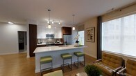 Located at 100 Danforth Ave in Dobbs Ferry, NY, this well-appointed 2-bedroom, 2-bathroom residence offers a thoughtfully designed single-floor layout with modern finishes and a welcoming ambiance. The open-concept living and kitchen area serves as the heart of the home, seamlessly connecting functional and social spaces. The kitchen is a standout feature, showcasing a large center island with a white quartz countertop and seating for multiple guests, complemented by a mix of white upper cabinetry and rich dark wood lower cabinets. Stainless steel appliances, a mosaic tile backsplash, and stylish pendant lighting add a polished, contemporary feel. Warm hardwood flooring runs throughout the main living area, enhancing the bright and airy atmosphere created by large windows that allow generous natural light to fill the space. The living area provides a comfortable retreat with tasteful décor and elegant drapery framing the windows. The two bedrooms offer private, restful spaces, while the two full bathrooms provide added convenience for residents and guests alike. Overall, this residence combines modern design sensibilities with practical living, making it an inviting and functional home in the heart of Dobbs Ferry.