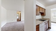 Located at 581 Lake Forest Dr in Norton Shores, Michigan, this single-floor, 3-bedroom, 2-bathroom home offers a practical and functional layout designed for comfortable everyday living. The galley-style kitchen is well-appointed with warm wood cabinetry lining both sides, light countertops, a double-basin sink, and white appliances including a range and refrigerator, complemented by durable wood-look flooring. The kitchen opens toward a dedicated dining area, creating a cohesive space for meals and gatherings. The living area is generously proportioned with neutral carpet, crisp white walls, and a hallway that connects to all three bedrooms. Each bedroom features soft carpeting and windows with blinds that bring in natural light and views of surrounding greenery. The bedrooms include closet storage, with at least one featuring a full reach-in closet with built-in shelving and a hanging rod. The two bathrooms are cleanly designed, each with warm wood vanities, light countertops, and large mirrors. The full bathroom includes a tiled tub-surround and wood-look flooring. Two hallways provide smooth circulation throughout the home, keeping the layout organized and accessible.