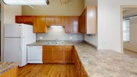 Located at 315 King St in downtown La Crosse, Wisconsin, this single-floor unit showcases a distinct urban loft aesthetic rooted in industrial design. Exposed metallic ductwork runs throughout the space, complementing the neutral palette of cream-toned walls and adding a raw, architectural character consistent with converted commercial buildings.

The main living area is generously proportioned, featuring wall-to-wall carpeting that softens the industrial elements above. Large, double-pane windows fitted with horizontal blinds allow abundant natural light to filter in while offering views of the surrounding downtown streetscape. A ceiling fan provides additional comfort and visual interest overhead.

The kitchen is thoughtfully appointed with warm honey-toned wood cabinetry, granite-look laminate countertops offering ample prep space, a double-basin sink, and a dishwasher. Hardwood flooring grounds this area, distinguishing it from the carpeted living zones. Tall upper cabinets maximize storage capacity.

A secondary carpeted room, also featuring exposed ductwork and dual windows, provides flexible use as a bedroom or office. The bathroom includes a full soaking tub with shower, a generous vanity with wood cabinetry, a wide mirror, and neutral tile flooring, creating a clean and functional space. Overall, the unit balances industrial character with everyday comfort.