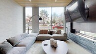 This single-floor space — associated with NorthPointe — showcases a refined, contemporary design that seamlessly blends contrasting materials and textures. Polished terrazzo floors run throughout, reflecting light and adding a sleek, upscale foundation to the interior.

The lounge area is anchored by expansive floor-to-ceiling windows that flood the space with natural light and frame views of the surrounding landscape. A warm wood-slatted ceiling adds organic warmth, while a dramatic textured dark stone accent wall provides bold visual contrast. Generous sectional seating and a low-profile round coffee table create an inviting, open atmosphere.

Adjacent to the lounge, a round dining table surrounded by leather chairs sits beneath a sculptural pendant light, again framed by a large window that connects the interior to the outdoors.

The wet bar area is a standout feature, finished with rich wood cabinetry, a white countertop island with bar stools, and a vibrant teal subway tile backsplash. Globe pendant lights cascade above, adding a mid-century modern touch. Open shelving and a beverage cooler complete the bar setup.

Together, these elements create a sophisticated, welcoming communal environment with a strong architectural identity.
