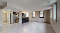 This single-floor, one-bedroom, one-bathroom unit offers a thoughtfully designed open-concept layout that maximizes its generous footprint. Light-toned tile flooring extends throughout the main living areas, creating a cohesive and airy atmosphere. Large windows with dark frames allow natural light to fill the space while framing views of the surrounding urban cityscape.

The kitchen is a standout feature, equipped with rich dark espresso cabinetry, stainless steel appliances including a refrigerator, gas range, and built-in microwave, and stone-finish countertops. A peninsula with bar-height seating serves as a natural divider between the kitchen and the expansive living area, making the space ideal for both everyday living and entertaining.

The bedroom is generously sized, featuring multiple windows that continue the urban view theme and provide excellent natural light. Neutral warm-toned walls complement the flooring throughout.

The bathroom is efficiently designed with a dark vanity cabinet, stone-finish countertop, undermount sink, and a glass-enclosed walk-in shower, all finished with the same light tile flooring found in the rest of the unit. The overall aesthetic is modern and cohesive.
