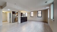 This single-floor, one-bedroom, one-bathroom unit offers a thoughtfully designed open-concept layout that maximizes its generous footprint. Light-toned tile flooring extends throughout the main living areas, creating a cohesive and airy atmosphere. Large windows with dark frames allow natural light to fill the space while framing views of the surrounding urban cityscape.

The kitchen is a standout feature, equipped with rich dark espresso cabinetry, stainless steel appliances including a refrigerator, gas range, and built-in microwave, and stone-finish countertops. A peninsula with bar-height seating serves as a natural divider between the kitchen and the expansive living area, making the space ideal for both everyday living and entertaining.

The bedroom is generously sized, featuring multiple windows that continue the urban view theme and provide excellent natural light. Neutral warm-toned walls complement the flooring throughout.

The bathroom is efficiently designed with a dark vanity cabinet, stone-finish countertop, undermount sink, and a glass-enclosed walk-in shower, all finished with the same light tile flooring found in the rest of the unit. The overall aesthetic is modern and cohesive.