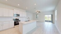 Located at 17224 Auburn Arch Loop in Wimauma, FL, this two-story home offers four bedrooms and three bathrooms across two well-organized floors. The ground floor hosts the open-concept kitchen and living area, garage, and one bedroom, while the upper floor accommodates the remaining bedrooms, bathrooms, hallways, a closet, and a laundry room.

The kitchen is a standout feature, showcasing crisp white shaker cabinetry, a white subway tile backsplash, stainless steel appliances, and a large center island with a built-in sink — all set atop light-toned tile flooring. A ceiling fan in the adjacent living area enhances the bright, airy atmosphere.

The primary bedroom is generously sized with a tray ceiling detail and direct access to a private en-suite bathroom, which features a glass-enclosed walk-in tile shower, dual-sink vanity with quartz countertops, and a window for natural light. A secondary bathroom offers a full soaking tub with classic white subway tile surround.

The additional bedrooms are well-proportioned, featuring either soft carpeting or light wood-look tile flooring and windows that invite natural light. The dedicated laundry room includes a full-size washer and dryer. The attached garage provides ample space and houses the home's water heater and electrical panel.