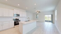 Located at 17224 Auburn Arch Loop in Wimauma, FL, this two-story home offers four bedrooms and three bathrooms across two well-organized floors. The ground floor hosts the open-concept kitchen and living area, garage, and one bedroom, while the upper floor accommodates the remaining bedrooms, bathrooms, hallways, a closet, and a laundry room.

The kitchen is a standout feature, showcasing crisp white shaker cabinetry, a white subway tile backsplash, stainless steel appliances, and a large center island with a built-in sink — all set atop light-toned tile flooring. A ceiling fan in the adjacent living area enhances the bright, airy atmosphere.

The primary bedroom is generously sized with a tray ceiling detail and direct access to a private en-suite bathroom, which features a glass-enclosed walk-in tile shower, dual-sink vanity with quartz countertops, and a window for natural light. A secondary bathroom offers a full soaking tub with classic white subway tile surround.

The additional bedrooms are well-proportioned, featuring either soft carpeting or light wood-look tile flooring and windows that invite natural light. The dedicated laundry room includes a full-size washer and dryer. The attached garage provides ample space and houses the home's water heater and electrical panel.