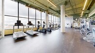 This state-of-the-art fitness center, spanning 154 square meters on a single floor, offers a comprehensive workout experience. Floor-to-ceiling windows flood the space with natural light and provide stunning city views, creating an inspiring exercise environment. The facility boasts an impressive array of equipment, including cardio machines, weight training apparatus, and functional fitness areas. High ceilings with exposed ductwork and suspended lighting give the space an industrial-chic aesthetic. The layout is thoughtfully designed, with different zones for various workout styles. Sleek tile flooring throughout ensures durability and easy maintenance. A large wall-mounted TV and vibrant wall art add visual interest and motivation. The gym's open plan and strategic placement of equipment maximize space utilization while maintaining a sense of openness, making it an inviting and efficient fitness destination.