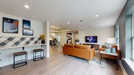 Located at 1707 Meadowlark Ct in Kansas City, KS, this single-floor community amenity space offers a thoughtfully designed environment built for both relaxation and activity. The open lounge area serves as the heart of the space, featuring light wood-look flooring, recessed lighting, and a warm, modern aesthetic. Cognac leather sofas anchor the seating area, complemented by a large wall-mounted television, a decorative chandelier overhead, and a bold teal accent wall framed by generous windows that flood the room with natural light. Adjacent to the lounge, a dining area with a sleek chandelier provides an inviting gathering spot. A standout wet bar area showcases striking geometric blue-and-white tile work as a full backsplash, paired with white shaker cabinets, a undermount sink, quartz countertops, and a beverage refrigerator — ideal for entertaining. The fitness center is well-equipped with treadmills, ellipticals, stationary bikes, and additional cardio machines, set against cool blue-gray walls with carpet tile flooring and natural light from multiple windows. A glass partition wall elegantly separates the fitness area from the lounge entry, which features a statement chandelier and French doors. A private meeting room with a round table and upholstered chairs rounds out the offerings, providing a quiet space for small gatherings or focused work sessions.